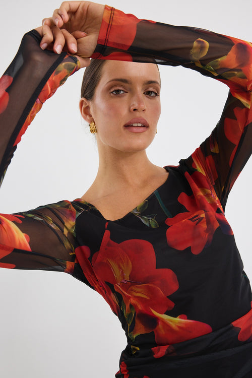 Woman wearing a fitted long sleeve mesh top with bold red floral print and sheer sleeves, paired with black jeans.
