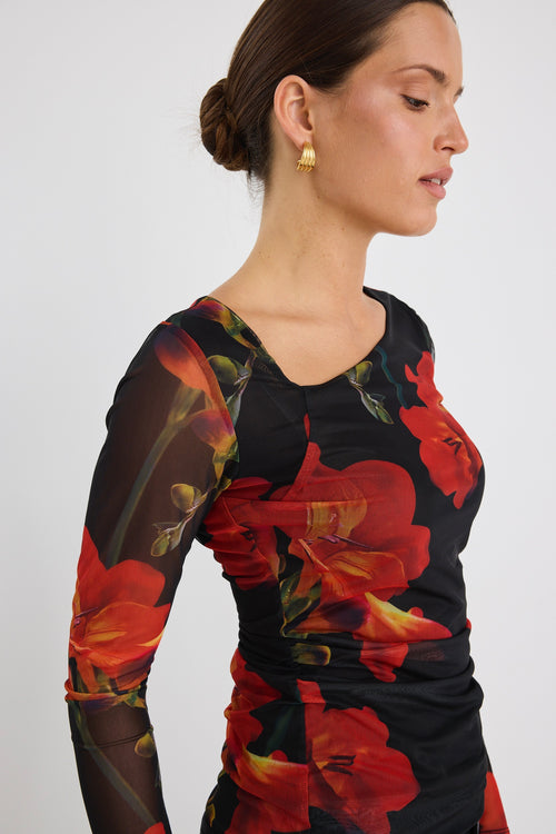 Woman wearing a fitted long sleeve mesh top with bold red floral print and sheer sleeves, paired with black jeans.