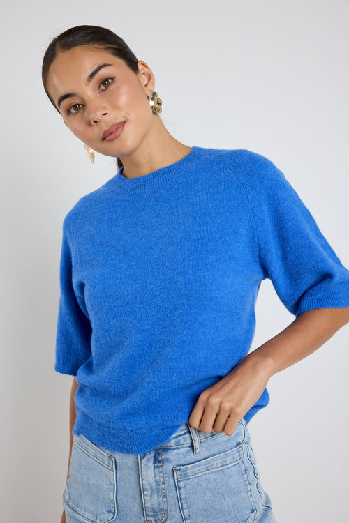 Model wears an azure blue knit tee with light blue jeans 