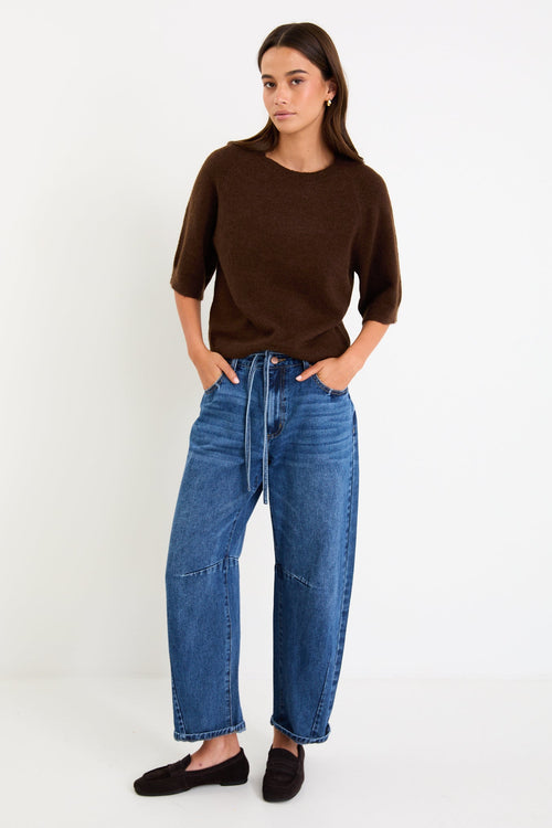 Woman wears a chocolate knit tee and blue jeans with brown loafers