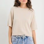 Woman wearing a beige sweater and blue jeans against a white background