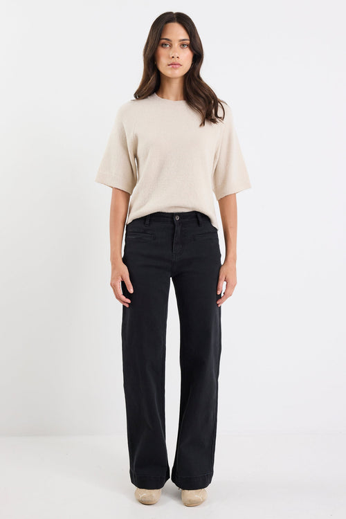 Woman wearing a beige sweater and black pants on a white background