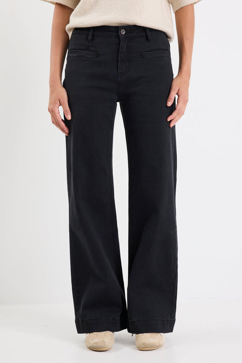 Person wearing black flared jeans and a beige top on a white background