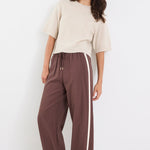 Woman wearing a beige top and brown pants with a white stripe on a white background