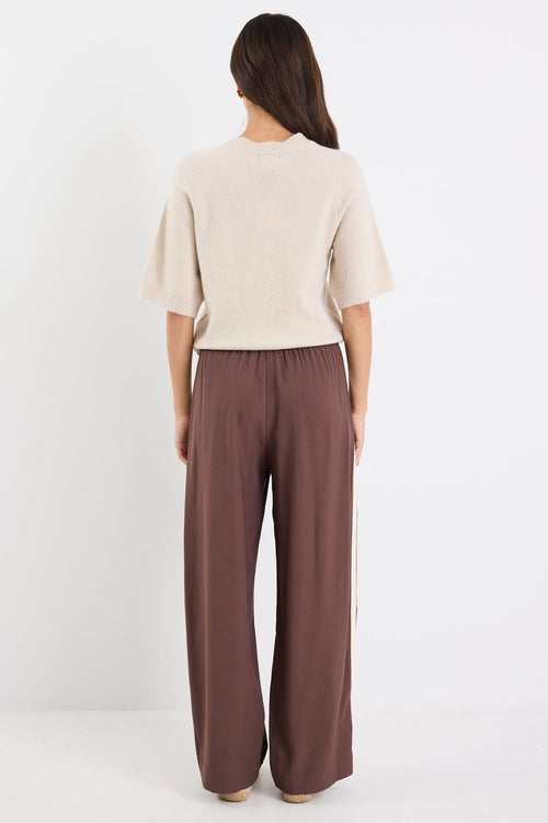 Woman wearing a beige top and brown pants on a white background