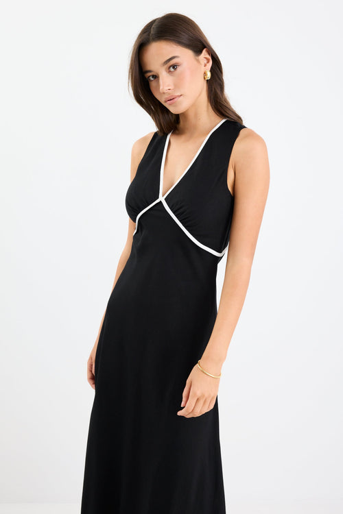 Woman wearing a black sleeveless maxi dress with a V-neckline, white contrast binding detail, bias cut, and softly flared hem.