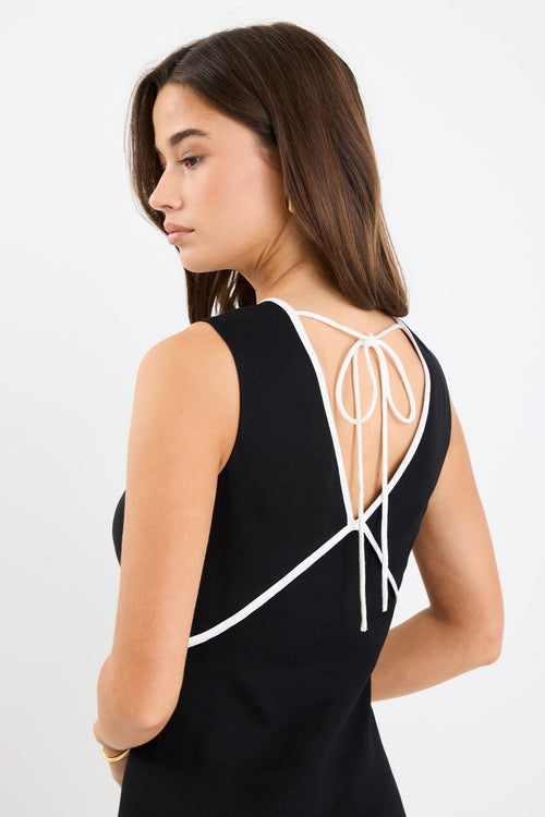 Woman wearing a black sleeveless maxi dress with a V-neckline, white contrast binding detail, bias cut, and softly flared hem.