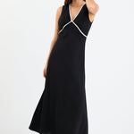 Woman wearing a black sleeveless maxi dress with a V-neckline, white contrast binding detail, bias cut, and softly flared hem.