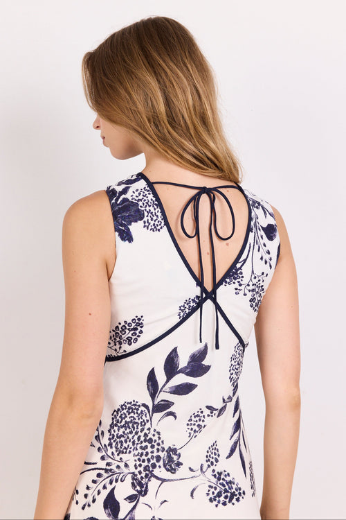 A woman shown from the back wearing a sleeveless white top with a navy blue floral print and a tie-back neckline.