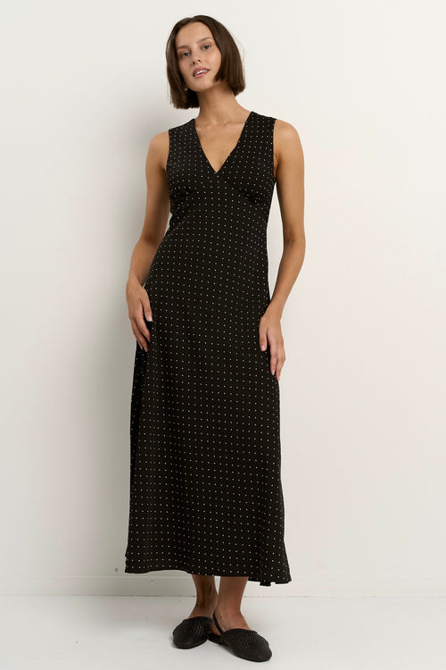 Woman wearing a sleeveless black midi dress with a V-neckline and small white polka dots, styled in a softly flowing silhouette.