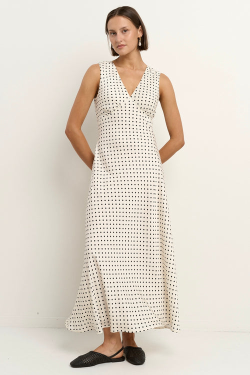 Woman wearing a sleeveless white midi dress with a V-neckline and small black polka dots, styled in a softly flowing silhouette.