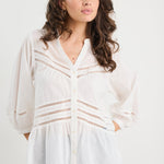 Woman wearing a white blouse with lace details and blue jeans on a white background