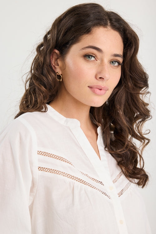 Woman with styled hair wearing a white blouse against a plain background