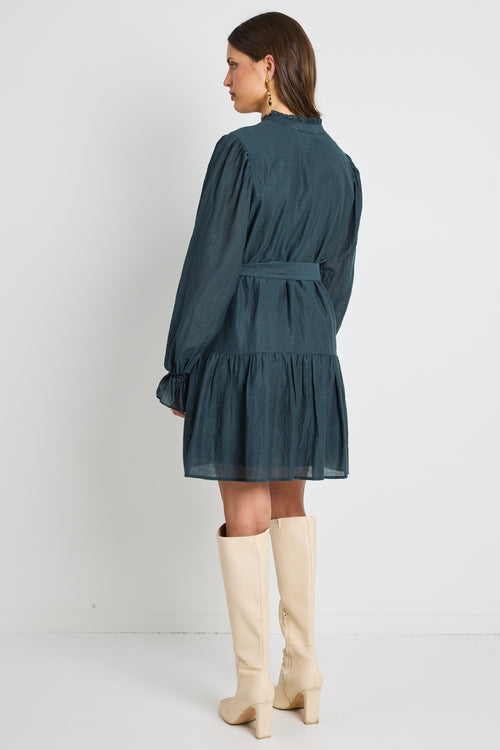 Model wears a long sleeve forest green mini dress with tie waist. 