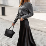 Woman in a gray sweater and black skirt walking on a sidewalk.