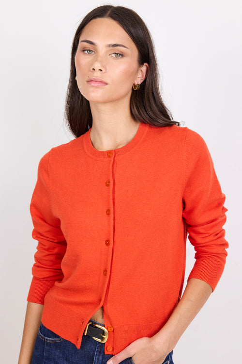 Person wearing an orange cardigan and dark blue jeans on a white background