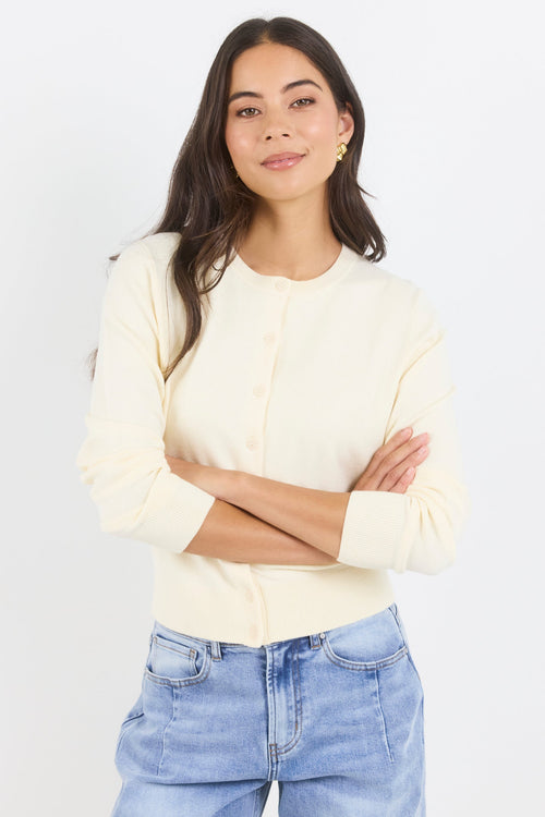 Woman wearing a light-colored blouse and blue jeans against a white background