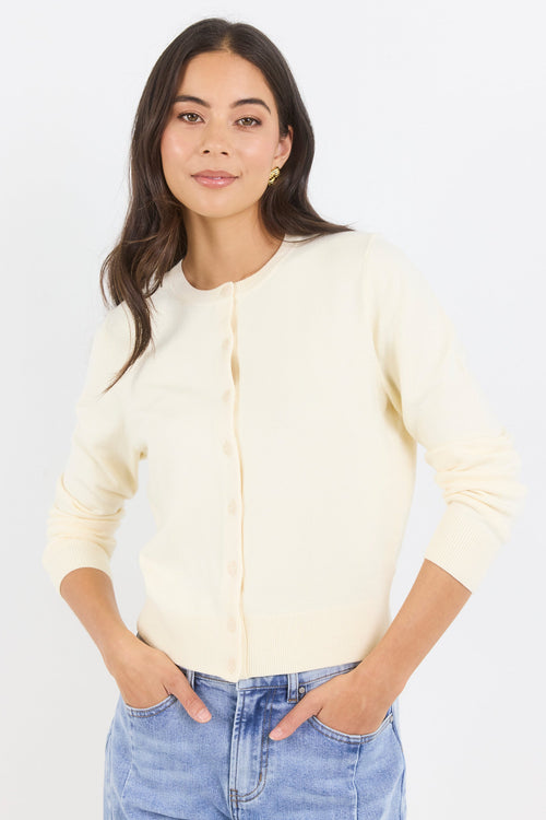 Woman wearing a light-colored cardigan and blue jeans against a white background