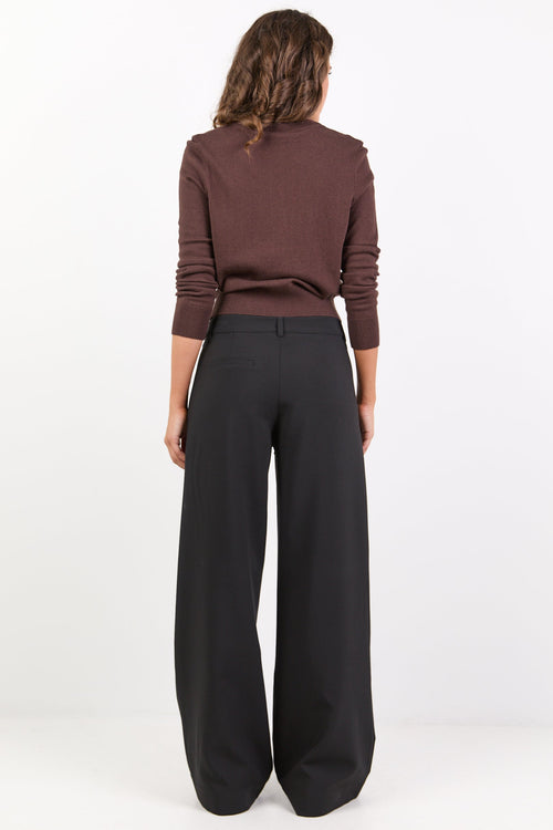 Person wearing a brown sweater and black pants on a white background