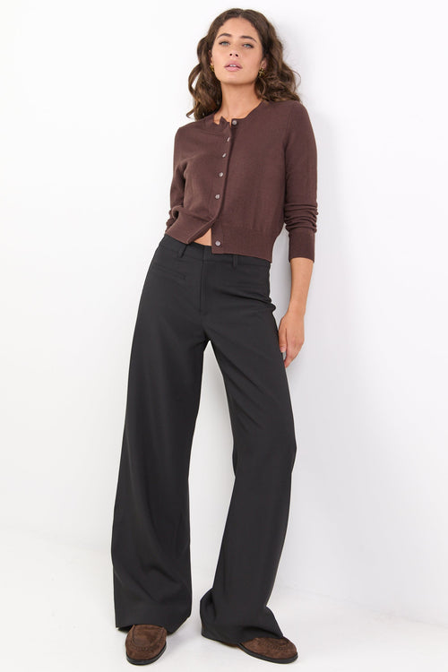 Woman wearing a brown cardigan and black pants against a white background