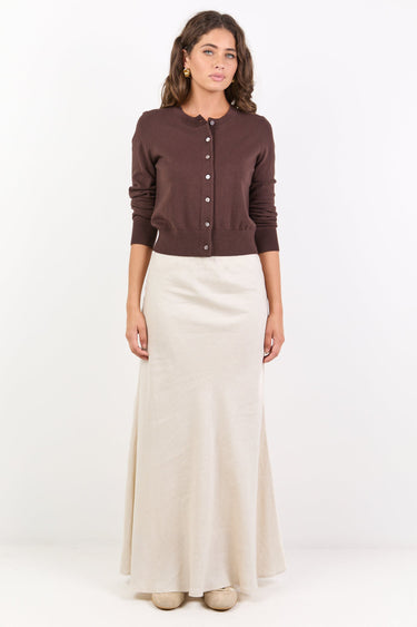 Woman wearing a brown cardigan and beige skirt on a white background