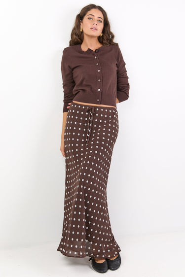 Woman wearing a brown button-up shirt and patterned skirt on a white background