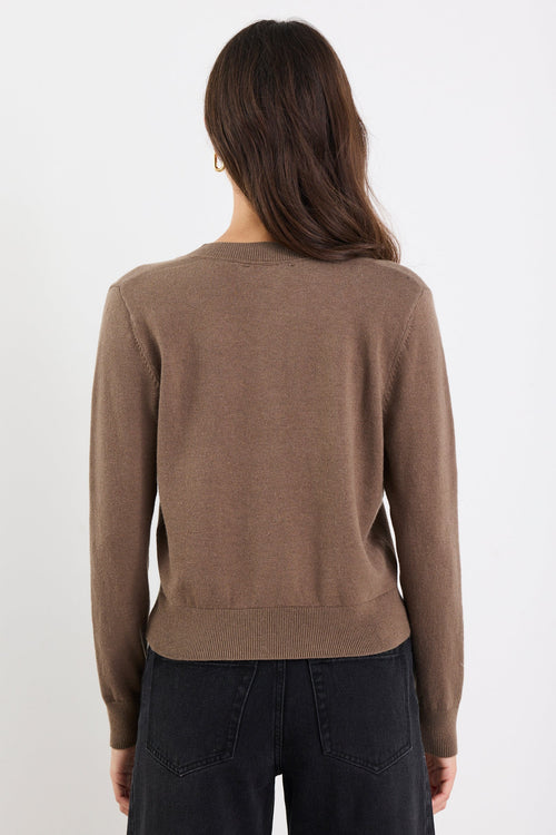Person wearing a brown sweater and black pants on a white background