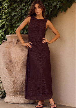 Woman in a dark dress standing against a textured wall with greenery