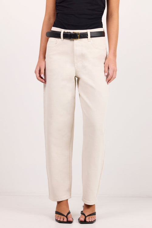 A model is shown from the waist down wearing a pair of cream jeans with a black belt, a black sleeveless top, and black sandals against a plain white studio background.