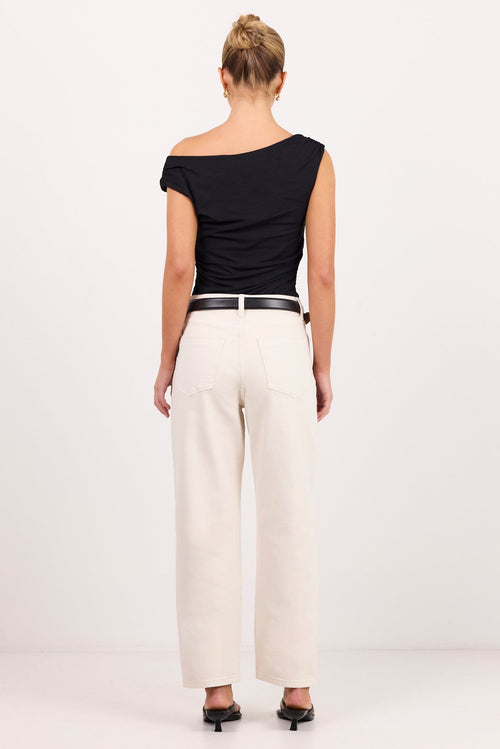 A woman viewed from the back wearing a black off-the-shoulder top and cream wide-leg jeans standing against a plain light studio background.