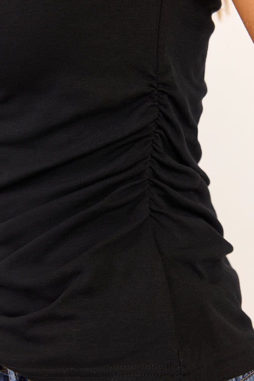 Close-up of a black ruched tank top with gathered detailing along the side, worn by a model against a plain light background.