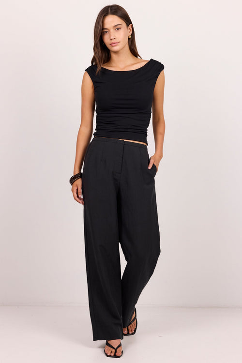 A woman modeling a black sleeveless top and black wide-leg trousers against a plain light studio background.