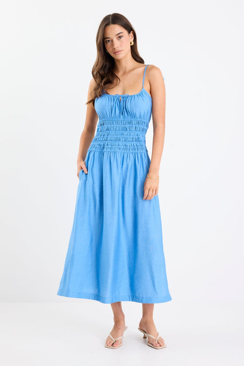 Woman wearing a bright blue strappy midi dress with tie-detail straps, shirred bodice, side split, and relaxed skirt.