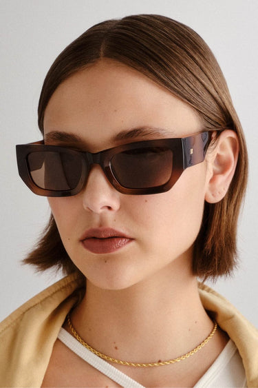 model wears Front-facing view of rectangular sunglasses featuring a matte tortoiseshell frame and warm brown polarised lenses. The angular design adds a bold, structured look, while the soft gradient effect on the frame enhances visual depth.