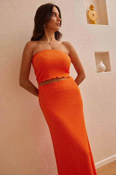 Model wearing orange bandeau top and maxi skirt set