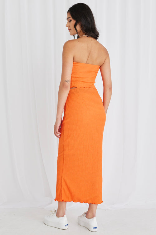 Model wearing orange bandeau top and maxi skirt set