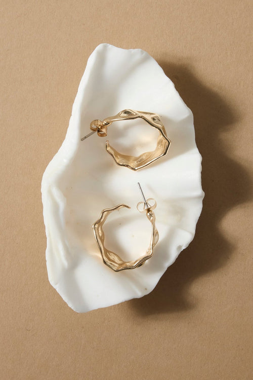 Gold hoop earrings on a white cloth against a beige background