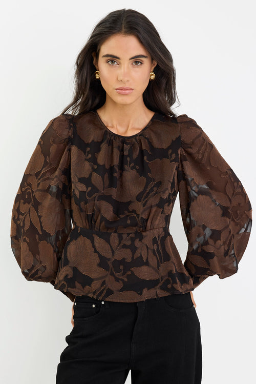 Woman wearing a brown floral blouse and black pants on a white background