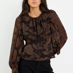 Woman wearing a brown floral blouse and black pants on a white background