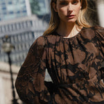 Woman wearing a patterned blouse standing outdoors with blurred background