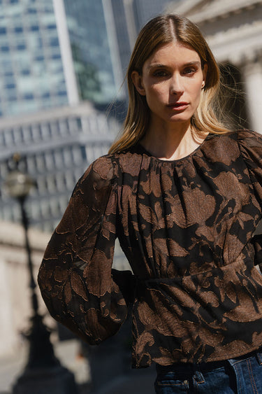 Woman wearing a patterned blouse standing outdoors with blurred background