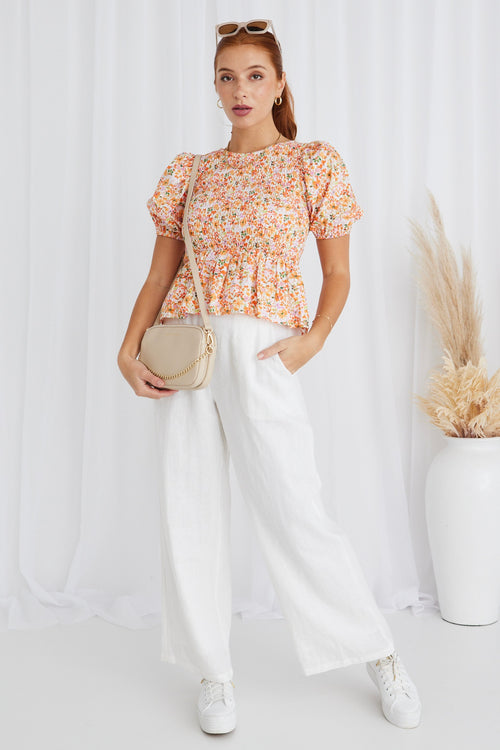 model in orange floral top and white pants and white sneakers