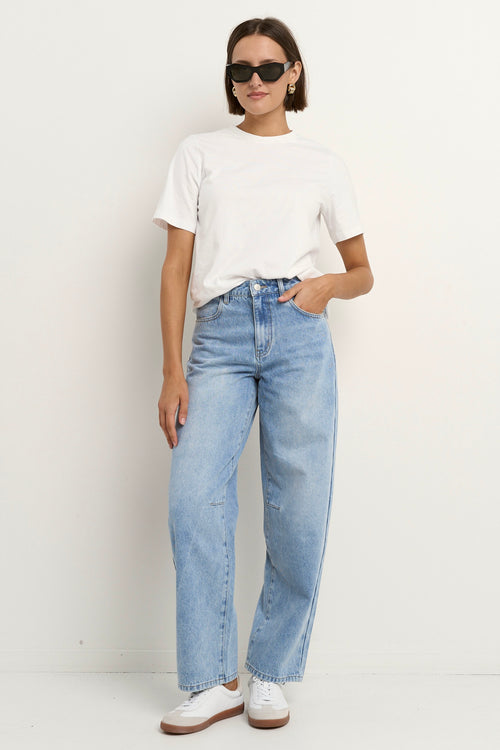 Woman wearing high-rise, light blue wide-leg jeans with a white tee and sneakers, styled in a relaxed, casual look.