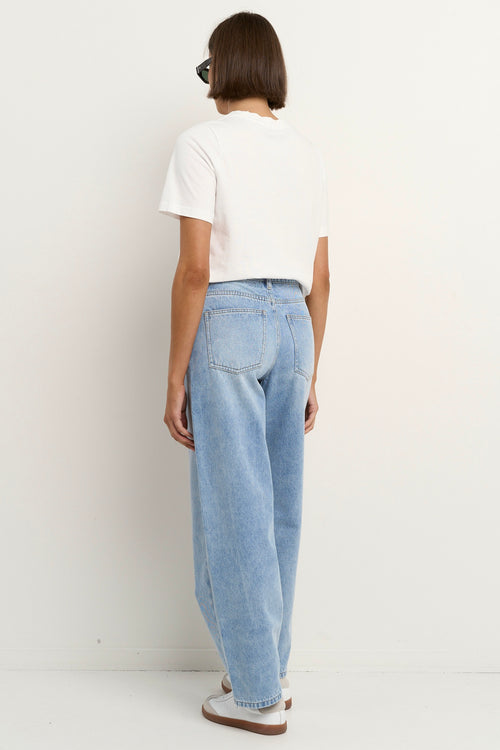 Woman wearing high-rise, light blue wide-leg jeans with a white tee and sneakers, styled in a relaxed, casual look.
