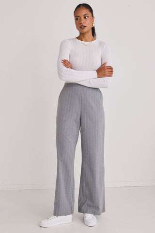 model wears white long sleeve top and grey pinstripe pants and white sneakers