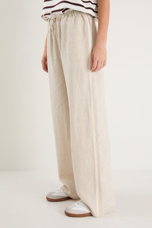 Woman in beige linen pants with side stripe detail and an elastic waistband, paired with a white stripe top. 