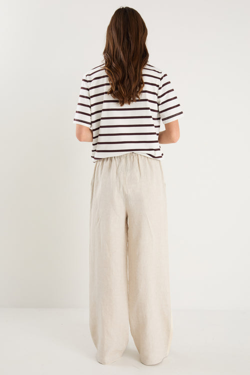 Woman in beige linen pants with side stripe detail and an elastic waistband, paired with a white stripe top. 