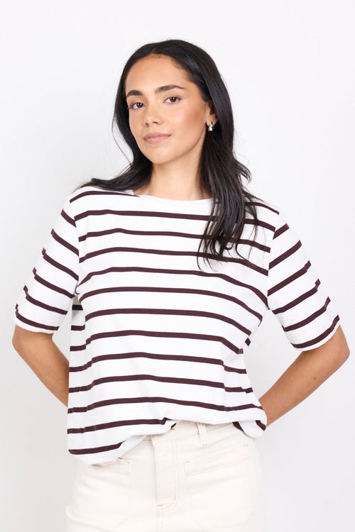 Woman wearing a black and white striped shirt with white pants on a white background