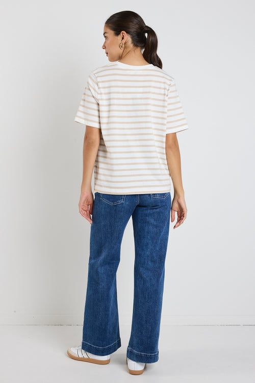 Model wears a white and ecru stripe shirt with blue jeans 