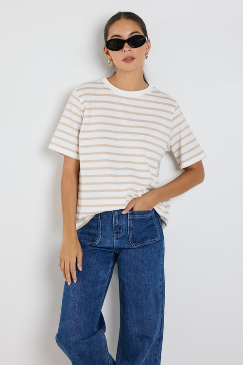 Model wears a white and ecru stripe shirt with blue jeans 